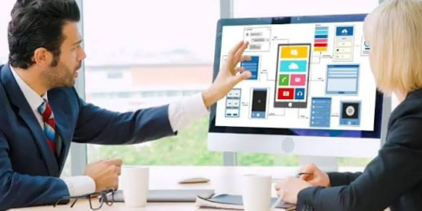 Two colleagues reviewing a custom app layout on a large monitor