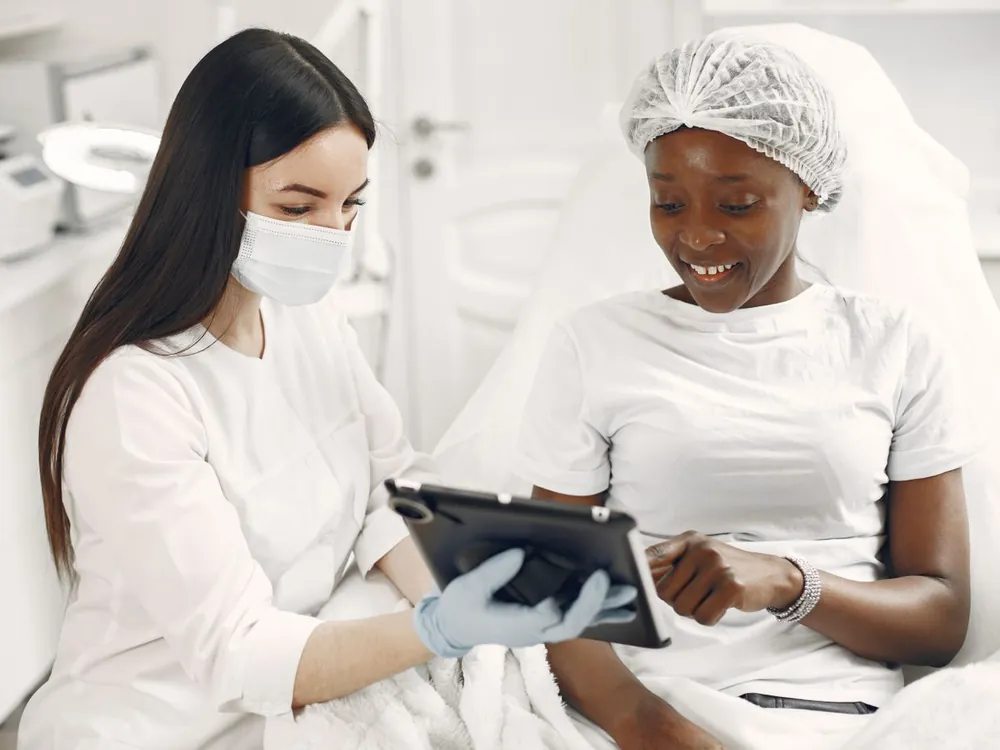 A dermatologist and a smiling patient looking at a tablet together in a skin clinic